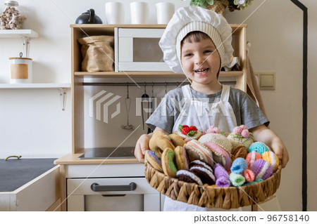Cute little baby boy in chef hat and apron playing at childish kitchen cooking food back view 96758140