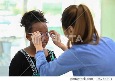 Cute little girl testing new glasses with optometrist in optical store. Eyesight and vision concept Cute little girl testing new glasses with optometrist in optical store. Eyesight and vision concept 96758204