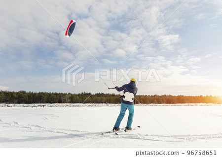 Panoramic view of many people friends enjoy riding kite surf board in warm suit on bright sunny winter day at frozen lake field snowy surface. Wintersport adrenaline fun adventure hobby acitivity Panoramic view of many people friends enjoy riding kite surf board in warm suit on bright sunny winter day at frozen lake field snowy surface. Wintersport adrenaline fun adventure hobby acitivity 96758651