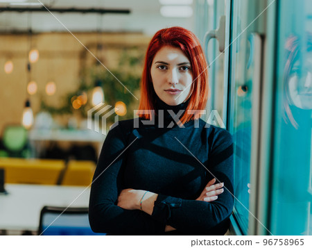 Headshot portrait of a modern woman with crossed arms in the office at night by the window 96758965
