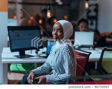 Business education and office concept. African American businesswoman wearing a hijab working, typing on a computer. Female entrepreneur sitting on her desk. Business education and office concept. African American businesswoman wearing a hijab working, typing on a computer. Female entrepreneur sitting on her desk. 96758987