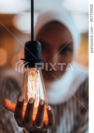Sentimental portrait of African-American young female Muslim wearing hijab while holding a lightbulb. 96759008