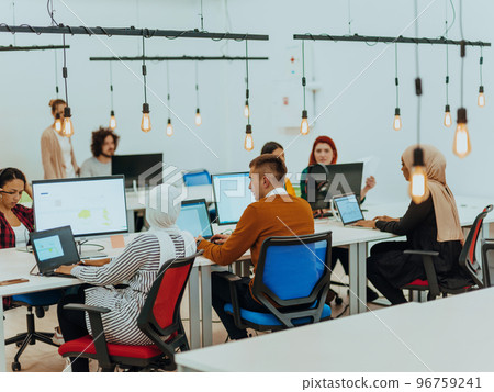 Group of multi-ethnic colleagues working on desktop computers, laptop and sharing their ideas in a modern office space.Young influencers work on online marketing projects. 96759241