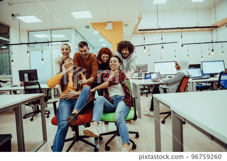 Team building and office fun. Young cheerful businesspeople in smart casual wear having fun while racing on office chairs and smiling. 96759260