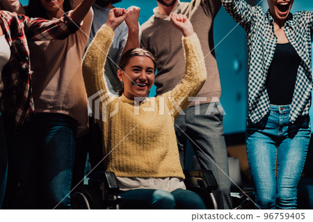 Photo of business women in wheelchairs with their hands raised in the air with their colleagues, together celebrating business success Photo of business women in wheelchairs with their hands raised in the air with their colleagues, together celebrating business success 96759405