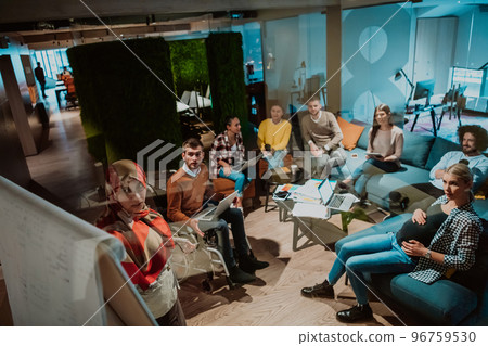 An older Muslim businesswoman presents a project to a young diverse team of people in a modern office 96759530