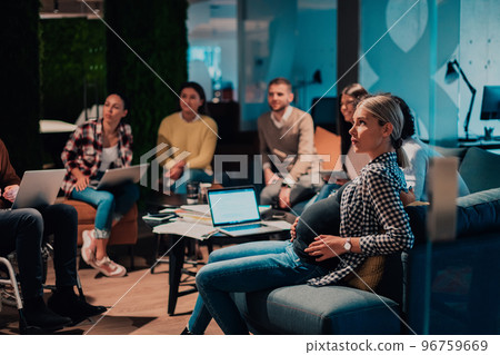 Pregnant woman sitting on the sofa of a modern office surrounded by colleagues  96759669