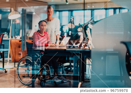 Businesswoman in a wheelchair working in a creative office. Business team in modern coworking office space. Colleagues working in the background at late night. 96759978