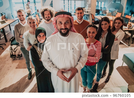 A diverse group of successful business people in a modern glass office stand together at the top with their Arab leader director 96760105
