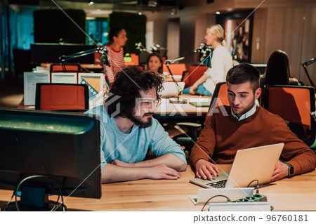 Two business friends discuss a joint project while using a laptop in a fashionable office Two business friends discuss a joint project while using a laptop in a fashionable office 96760181