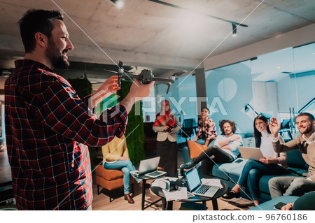 A bearded man in a modern office explaining to his young diverse team how a drone working  96760186