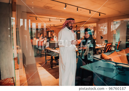 Portrait photo of Arab leader businessman with muslim hijab woman discussing business projects while using tablets and smartphone in modern glass office  96760187