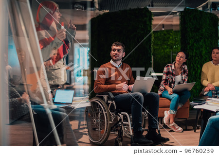 An older Muslim businesswoman presents a project to a young diverse team of people in a modern office An older Muslim businesswoman presents a project to a young diverse team of people in a modern office 96760239