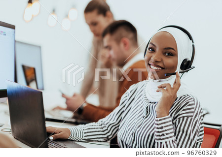 African American muslim woman with hijab and headset working as customer support in a modern office. African American muslim woman with hijab and headset working as customer support in a modern office. 96760329