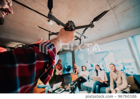 A bearded man in a modern office explaining to his young diverse team how a drone working A bearded man in a modern office explaining to his young diverse team how a drone working 96760386