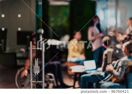Businesswoman in a wheelchair on break in a modern office with her team in the background 96760421