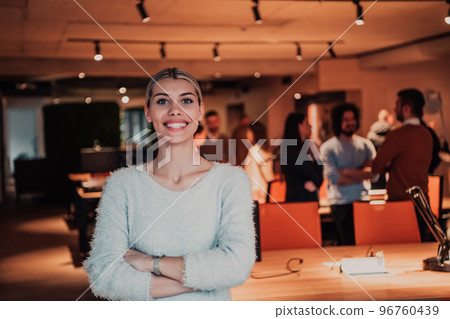 Portrait photo of a modern blonde on a break from work in a modern office. In the background, the team working on the projects 96760439