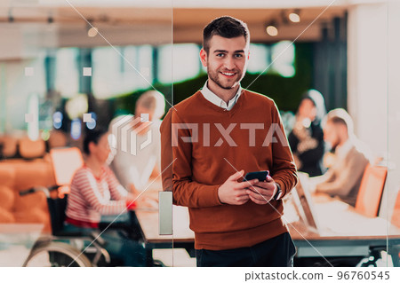 Handsome young business man standing confident in the office in front of his team Handsome young business man standing confident in the office in front of his team 96760545