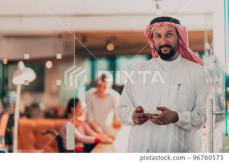 Middle eastern Arab businessman in the office speaking on smartphone in front of his team Middle eastern Arab businessman in the office speaking on smartphone in front of his team 96760573