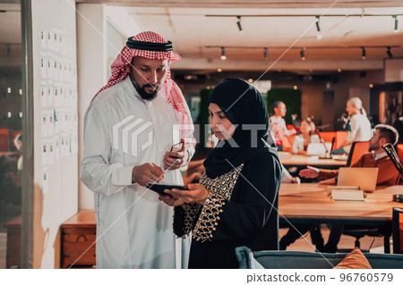 Portrait photo of Arab leader businessman with muslim hijab woman discussing business projects while using tablets and smartphone in modern glass office  96760579