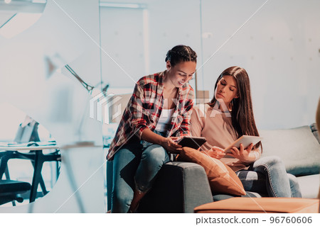 Two young women in a modern office solve a problem together while using a laptop Two young women in a modern office solve a problem together while using a laptop 96760606