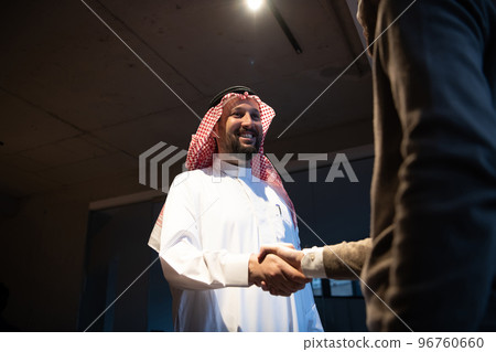An elderly Arab man shaking hands with a businessman and ending a business meeting with successful business deals 96760660