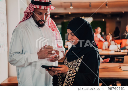 Portrait photo of Arab leader businessman with muslim hijab woman discussing business projects while using tablets and smartphone in modern glass office  96760661