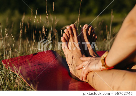 Close Up Unrecognisable Woman Holding Her Feet While Sitting on the Mat During Yoga Outdoors at Sunset 96762745