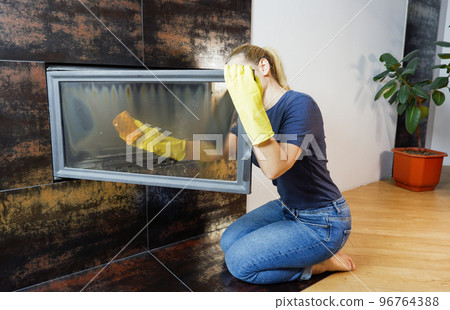 Homework. Young blonde woman in casual clothes cleans the fireplace. 96764388