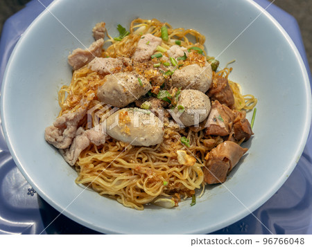 Egg Noodles with braised pork (stewed pork), fresh pork and pork balls without soup sprinkled with pepper and chopped onions in blue bowl. 96766048