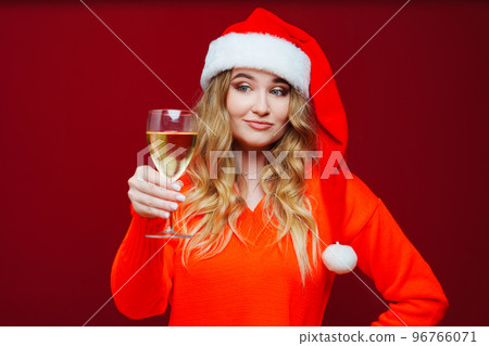 A beautiful woman in a Santa Claus hat with champagne on a red background. A beautiful woman in a Santa Claus hat with champagne on a red background. 96766071