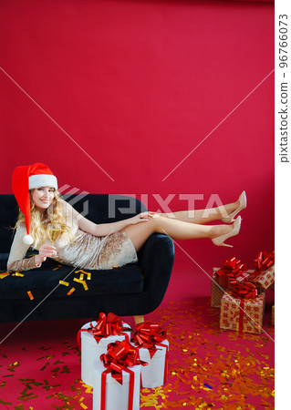 woman in santa hat with champagne and sparklers in red room on sofa with canfeti woman in santa hat with champagne and sparklers in red room on sofa with canfeti 96766073