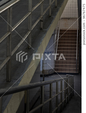 Stairs leading to interior view of public underpass with white tiled walls and CCTV. 96767475