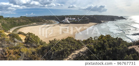 Panoramic view of Praia de Odeceixe Mar Surfer beach with golden sand, atlantic ocean waves, river bend and white houses of Odeceixe village. Rota Vicentina coast, Odemira, Portugal. 96767731