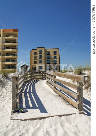 Sand covered wood pathway with handrails near the buildings against the clear blue sky at Destin, FL Sand covered wood pathway with handrails near the buildings against the clear blue sky at Destin, FL 96767962
