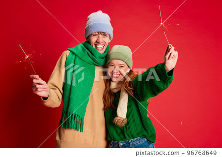 Portrait of young man and woman in green knitted sweater and hat posing with sparkles isolated over red background 96768649