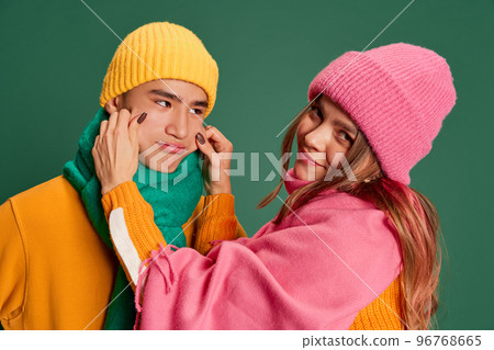 Portrait of young man and woman, lovely couple in bright knitted hat and scarf posing isolated over green background Portrait of young man and woman, lovely couple in bright knitted hat and scarf posing isolated over green background 96768665