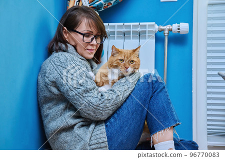 Woman in knitted woolen sweater with pet cat warming near heating radiator Woman in knitted woolen sweater with pet cat warming near heating radiator 96770083