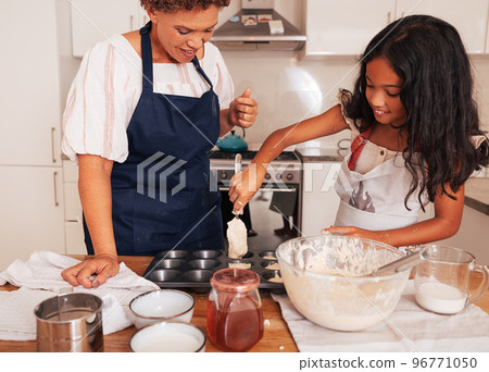 Smiling girl pouring batter from spoon. Granny and a granddaughter making cupcakes. Smiling girl pouring batter from spoon. Granny and a granddaughter making cupcakes. 96771050