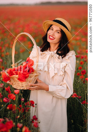 A girl in a white dress and with a basket of poppies walks through a poppy field A girl in a white dress and with a basket of poppies walks through a poppy field 96771080