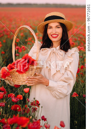A girl in a white dress and with a basket of poppies walks through a poppy field A girl in a white dress and with a basket of poppies walks through a poppy field 96771081