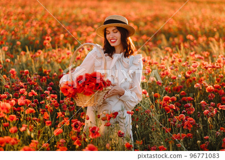 A girl in a white dress and with a basket of poppies walks through a poppy field A girl in a white dress and with a basket of poppies walks through a poppy field 96771083