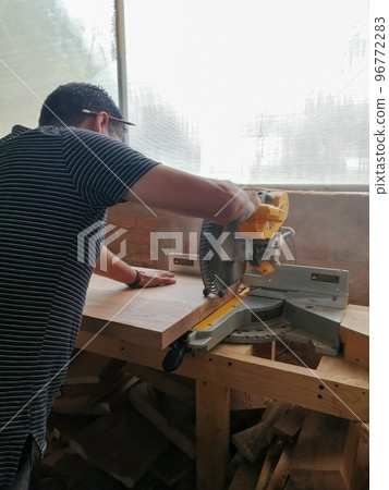 A man cuts wood on a circular saw in a joinery, band saw, holding a plank A man cuts wood on a circular saw in a joinery, band saw, holding a plank 96772283