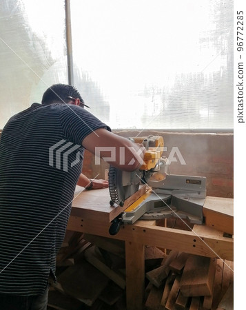 A man cuts wood on a circular saw in a joinery, band saw, holding a plank A man cuts wood on a circular saw in a joinery, band saw, holding a plank 96772285