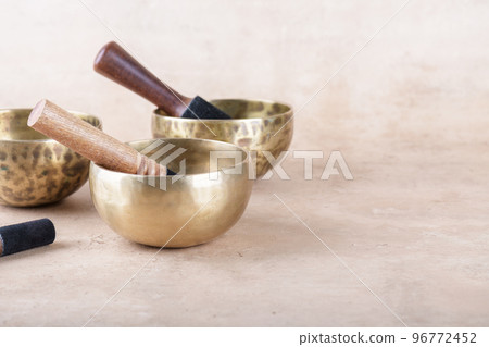 Tibetan singing bowls with sticks used during mantra meditations on beige stone background, copy space. 96772452