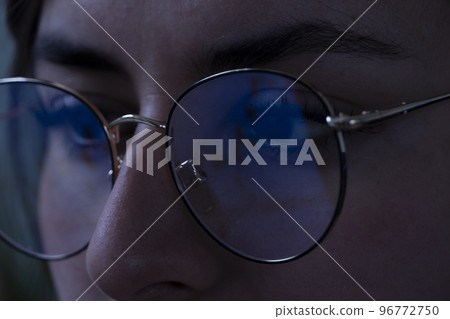 young woman, watching the stock market at night, the same market is seen in the reflection of her glasses 96772750