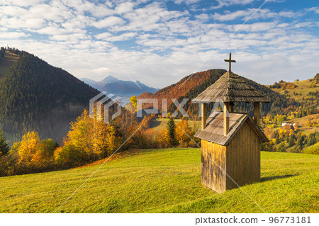 A small wooden bell tower in the foreground of a mountain land. 96773181