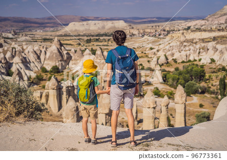 Father and son tourists exploring valley with rock formations and fairy caves near Goreme in Cappadocia Turkey Father and son tourists exploring valley with rock formations and fairy caves near Goreme in Cappadocia Turkey 96773361