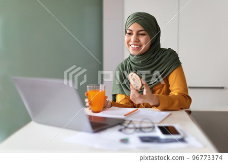 Young Muslim Woman Eating Snacks In Front Of Laptop At Home 96773374