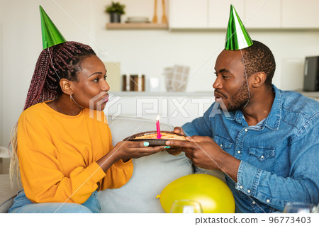 Young african american couple having cake while celebrating birthday and blowing candles together Young african american couple having cake while celebrating birthday and blowing candles together 96773403